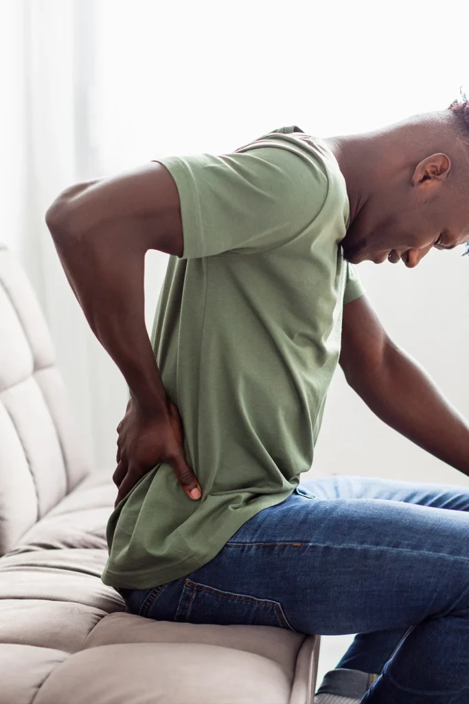 man is seated on couch holding lower back in pain