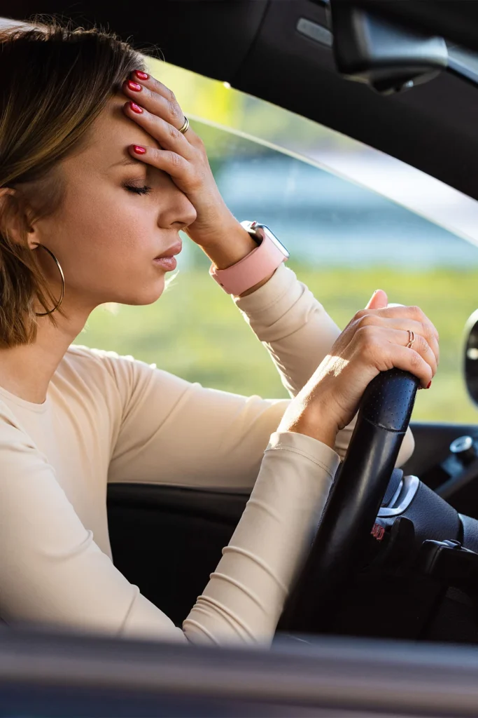 woman face palms in frustration in the driver's seat of a car